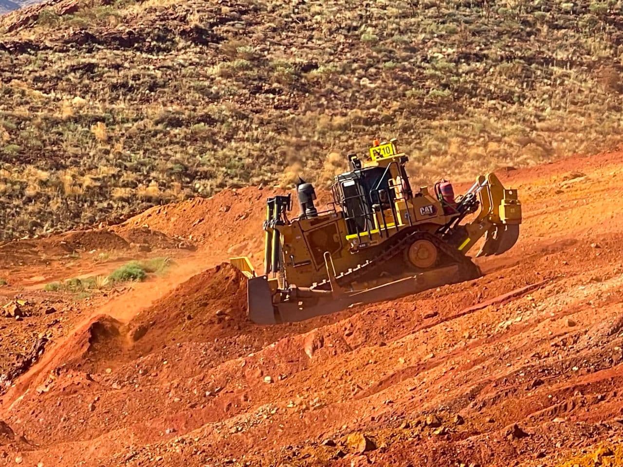 CAT dozer cutting a haul road into a red dirt hillside
