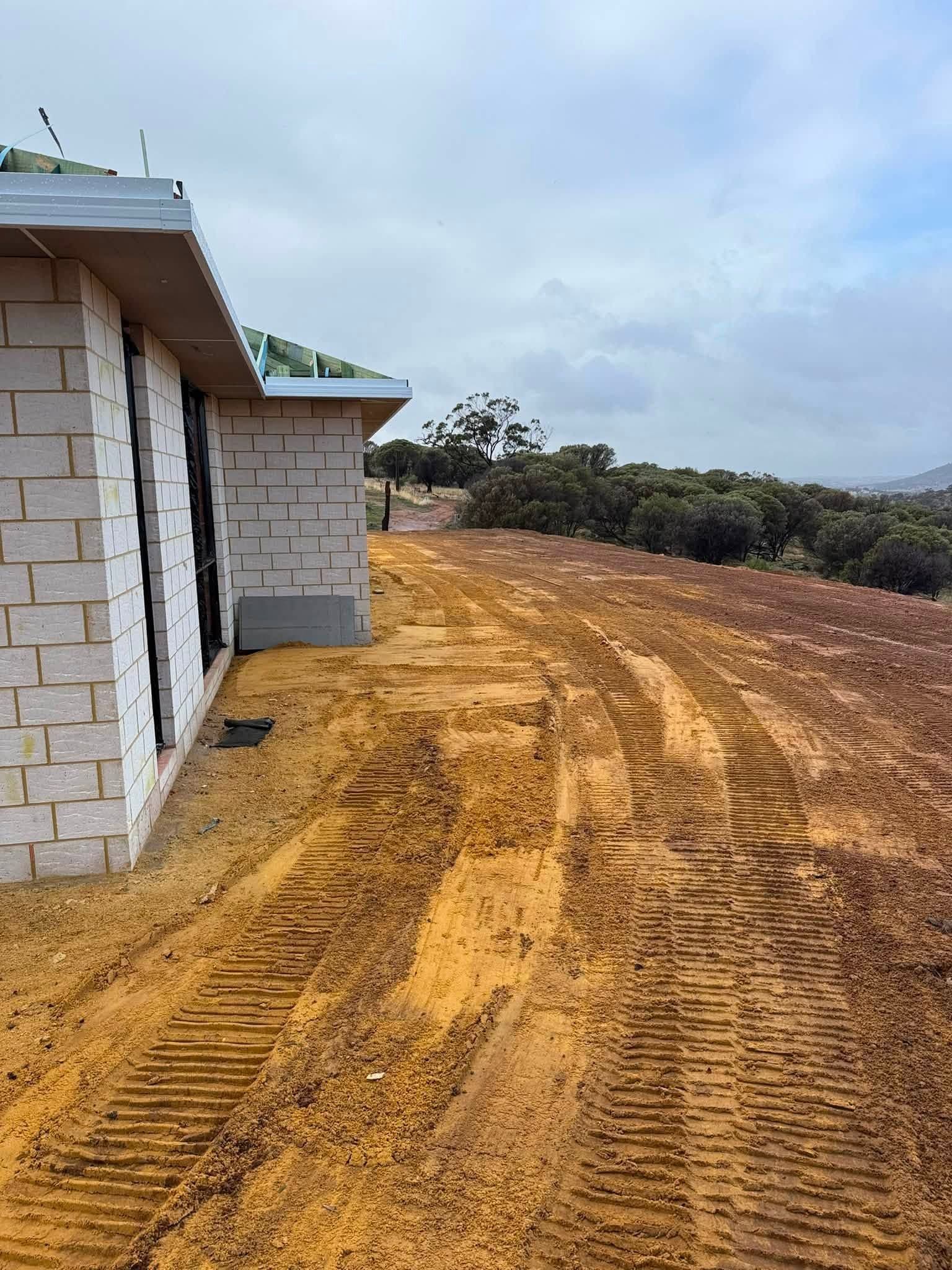 Red clay driveway cut and formed to a newly built home in the Perth hills, tracked flat under a clouded WA sky